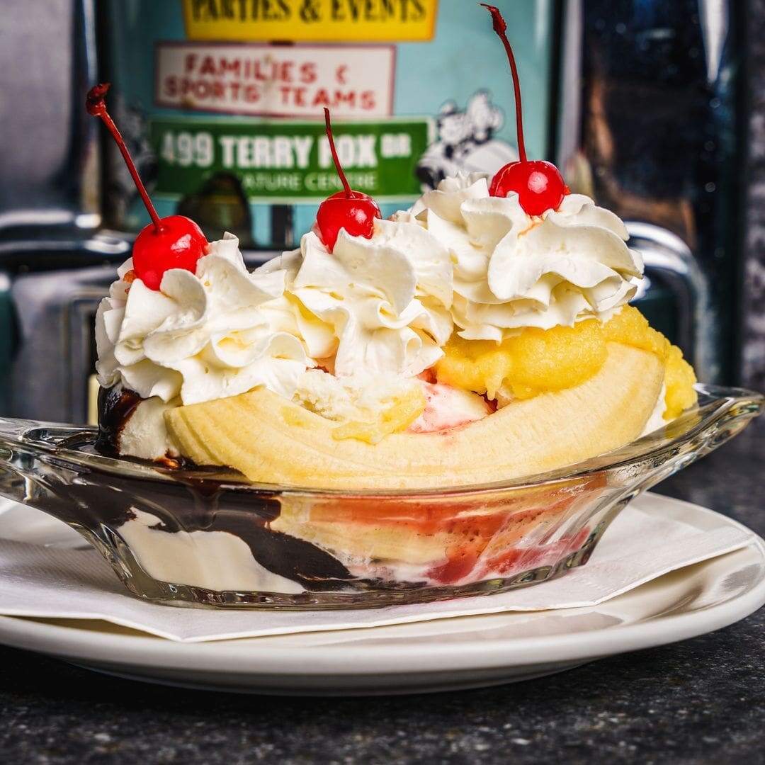 A long glass dish with a banana, three scoops of ice cream, chocolate sauce, whip cream and three cherries