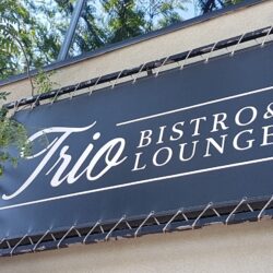 A black sigh on a white building with the business name Trio Bistro & Lounge
