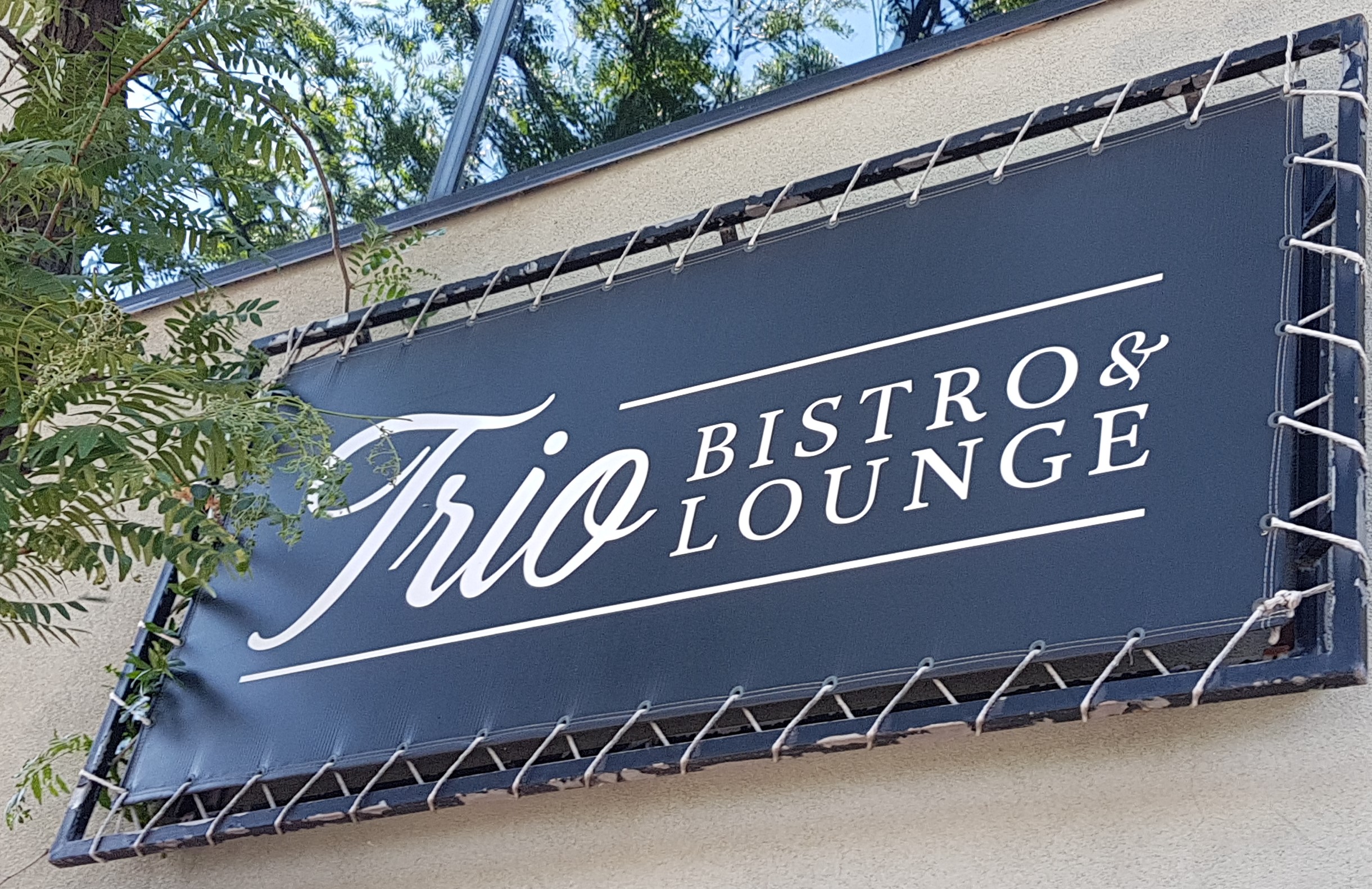 A black sigh on a white building with the business name Trio Bistro & Lounge