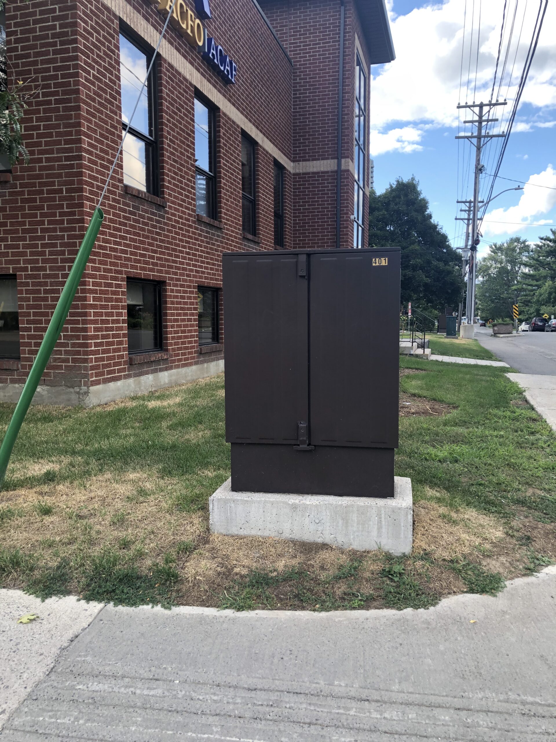A tall slim utility box on a concrete base at the corner of two roads