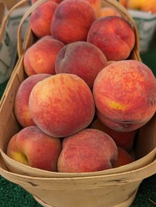 An image of several peaches in a wooden basket.