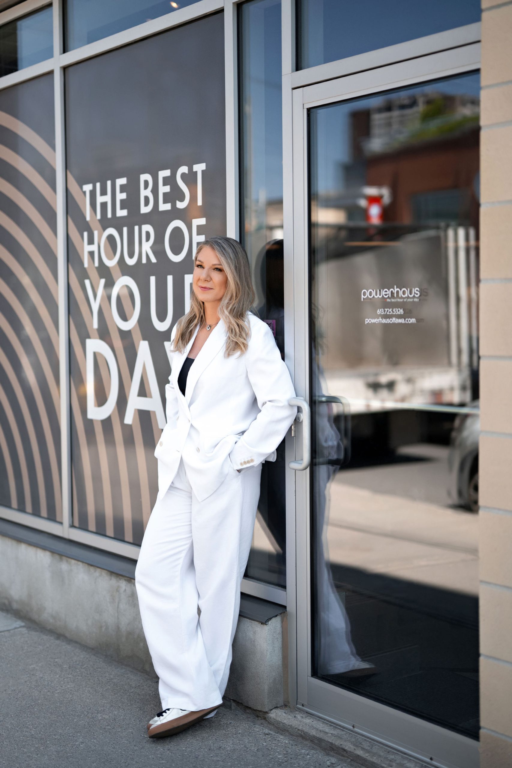 Siliva Klein, founder of Powerhaus in Westboro, stands in front of the powerhaus door in a white suit