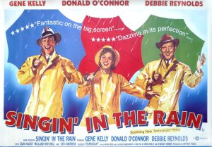 Three people in yellow rain jackets and blue, red and green umbrellas with the words Singin' in the Rain underneath them