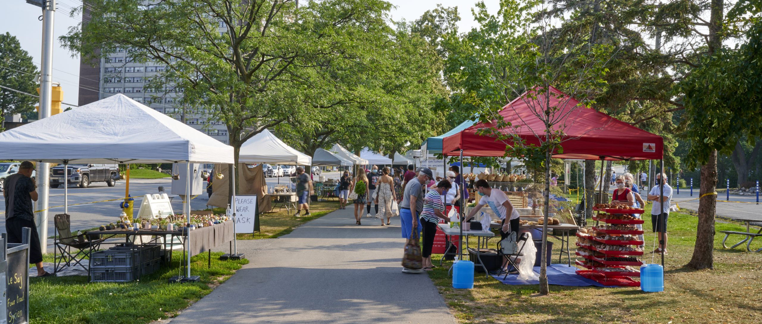A paved pathway lined with shade tents filled with farmers market produce. 
