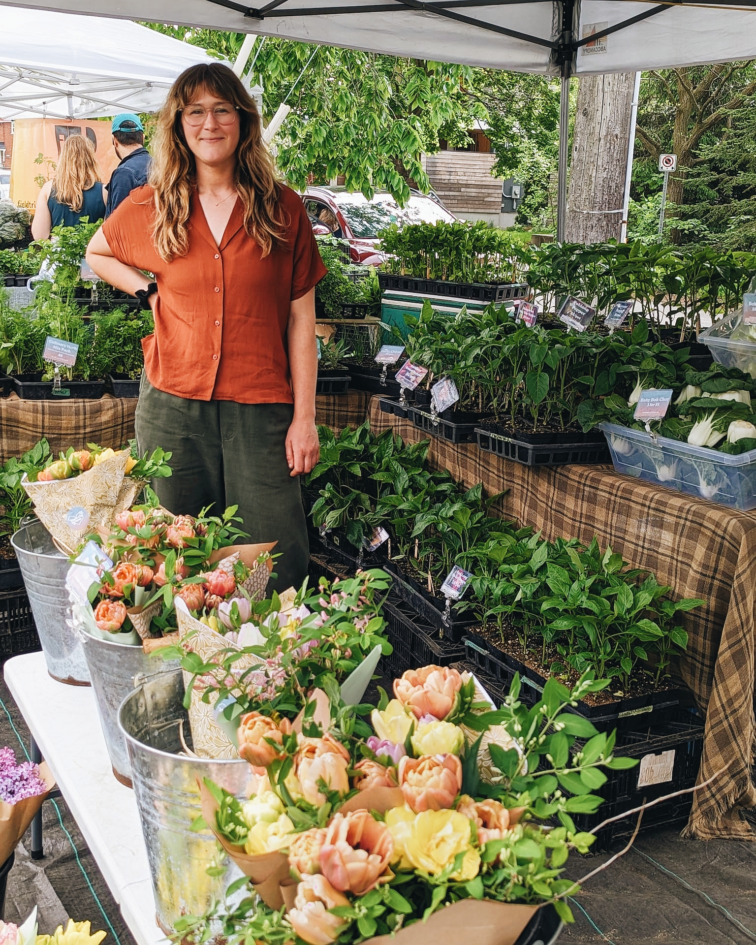 Woman with long hair in orange shirt standing in front of fresh flower stall
