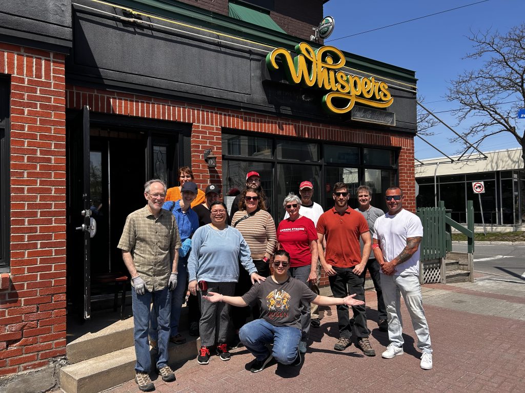 A group of people standing, smiling in front of Whispers Pub.
